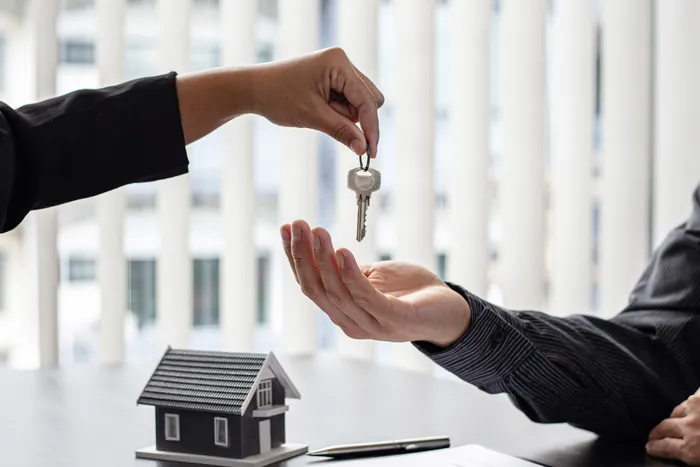 Successful home purchase or rental concept with a hand handing over keys above a miniature house model on a desk.