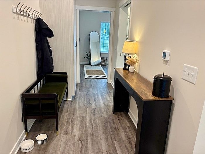 Welcoming apartment hallway with elegant wood flooring, contemporary console table, and cozy seating area, leading to a bright room with natural light.