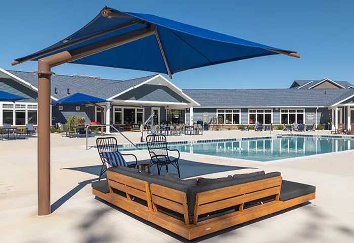 Luxurious outdoor pool area with elegant seating, shaded by chic blue umbrellas, set against a stylish modern building.