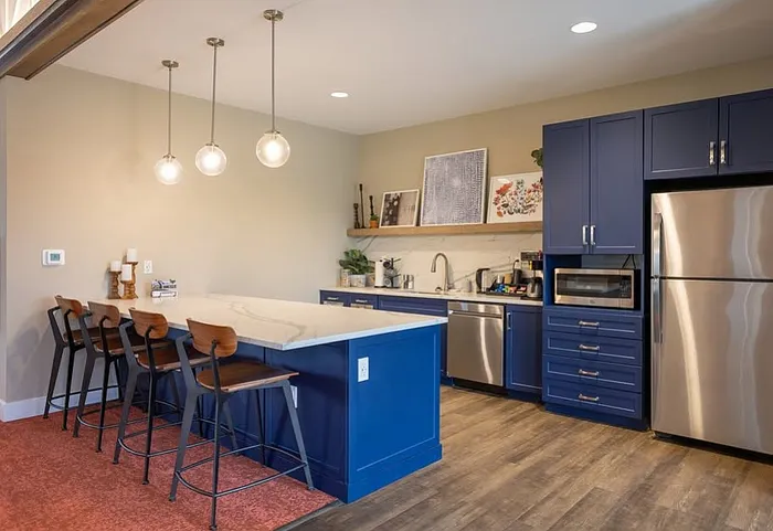 Chic modern kitchen featuring elegant blue cabinetry, sleek stainless-steel appliances, and a stylish breakfast bar with pendant lighting.