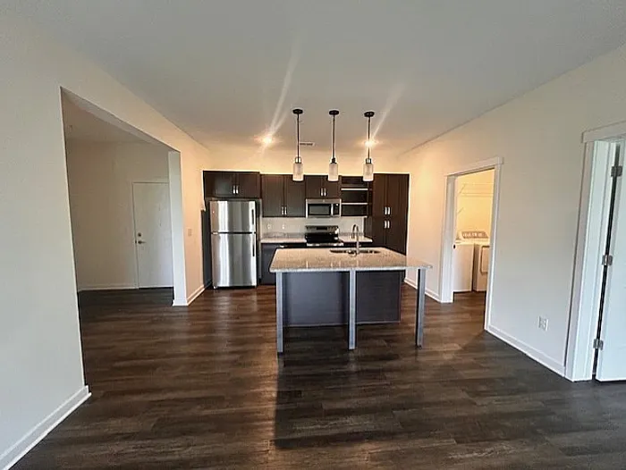 Modern apartment kitchen with sleek dark cabinets, stainless steel appliances, and a spacious island under stylish pendant lighting.