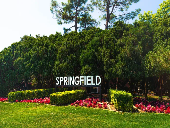Welcoming Springfield community entrance featuring lush greenery and vibrant flower beds.