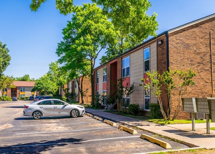 Bright and inviting suburban apartment complex with lush green trees and convenient parking.