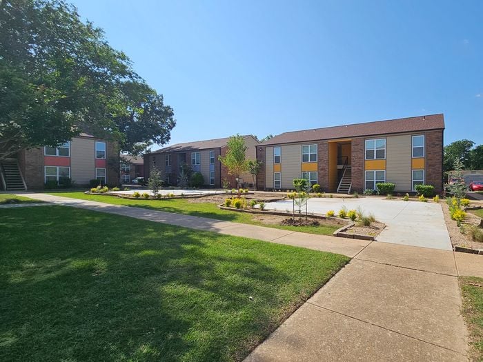 Sunny view of charming courtyard apartments with well-maintained green spaces and paved pathways.