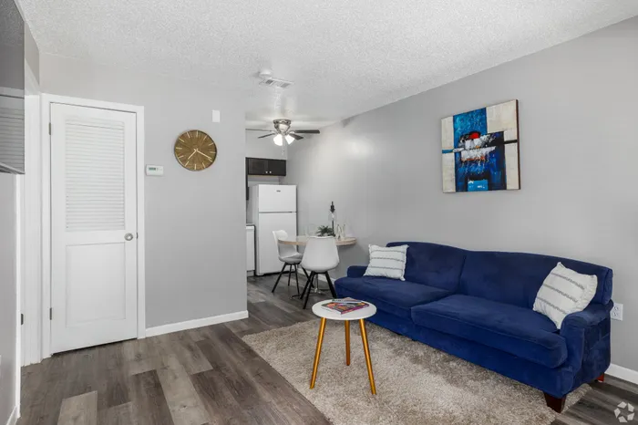 Inviting living area showcasing a plush blue sofa, stylish artwork, and cozy dining nook near an elegant ceiling fan.