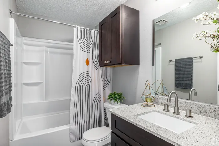 Modern bathroom with sleek granite countertop, stylish cabinetry, and elegant geometric shower curtain.