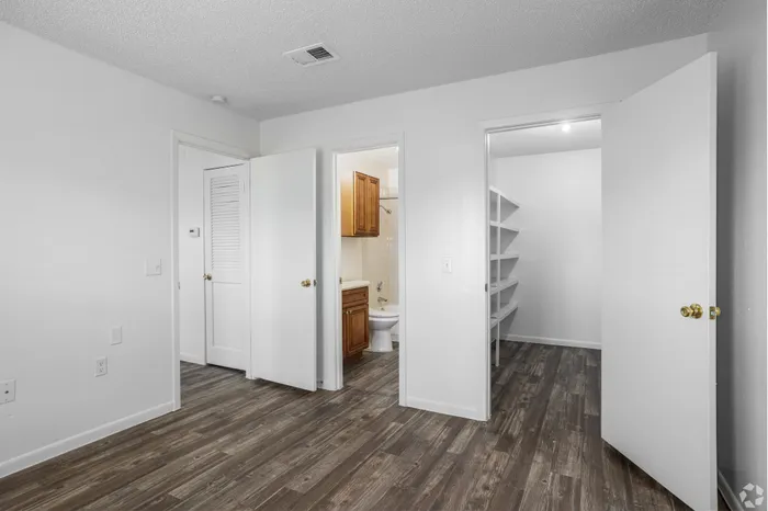 Modern interior showcasing a spacious room with elegant wood flooring, featuring an open walk-in closet and a glimpse of a stylish bathroom.