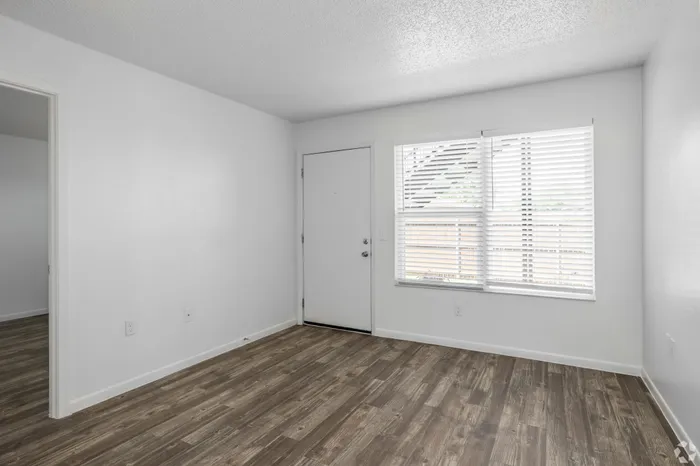 Bright and inviting room featuring sleek hardwood flooring, large window for natural light, and modern white walls.