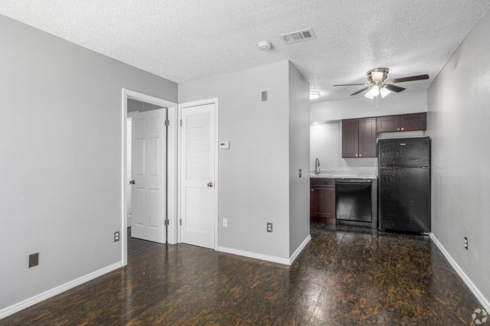 Modern living space featuring sleek hardwood floors, an open-plan kitchen with elegant dark cabinetry, and ambient recessed lighting.
