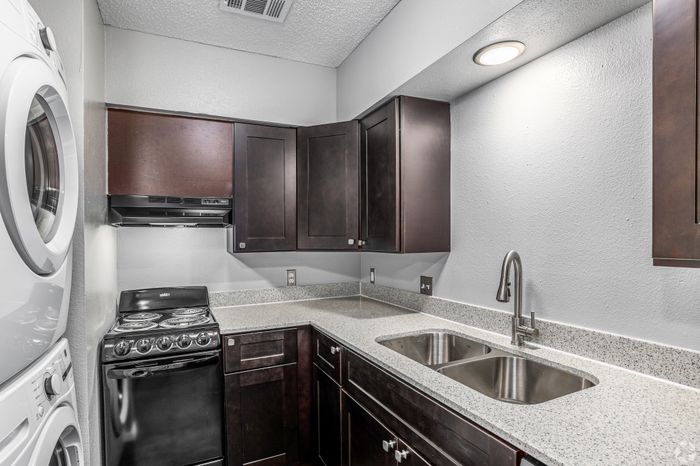 Modern compact kitchen with sleek dark cabinets, stainless steel sink, and in-unit washer and dryer for convenience.