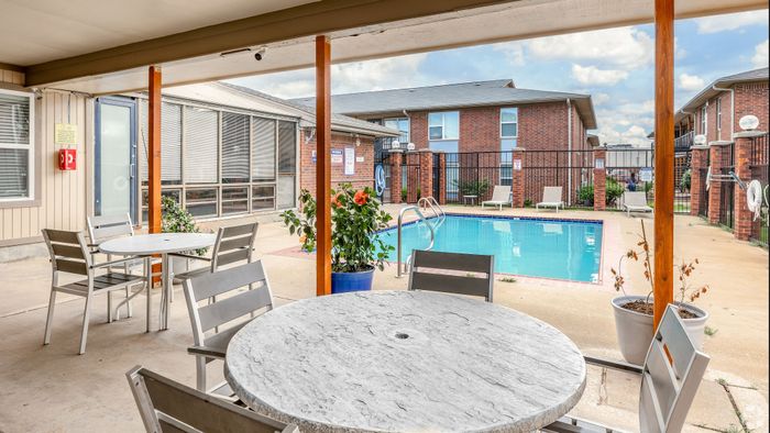 Inviting outdoor patio area with stylish seating overlooking a pristine swimming pool, perfect for relaxation and leisure in a charming apartment complex.