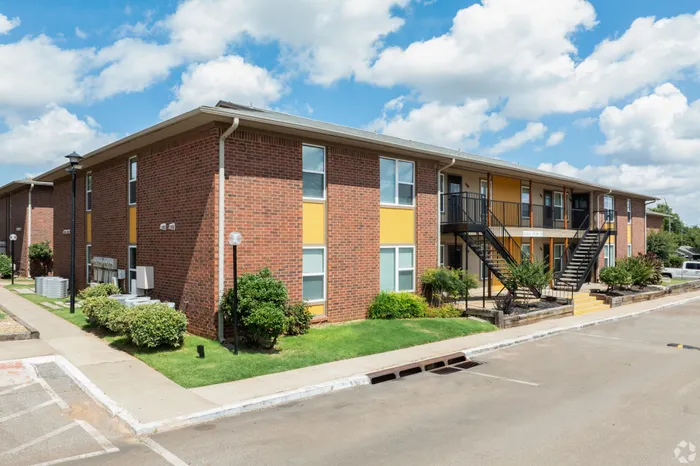 Charming two-story brick apartment building with vibrant accents, surrounded by lush greenery and clear blue skies.