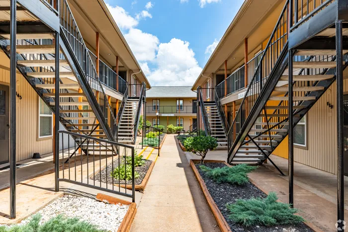 Charming apartment complex with modern exterior, featuring welcoming landscaped pathways and elegant staircases under a bright blue sky.