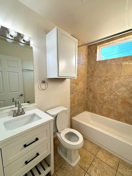 Bright bathroom featuring elegant tile work, modern vanity with under-sink storage, and sleek fixtures.