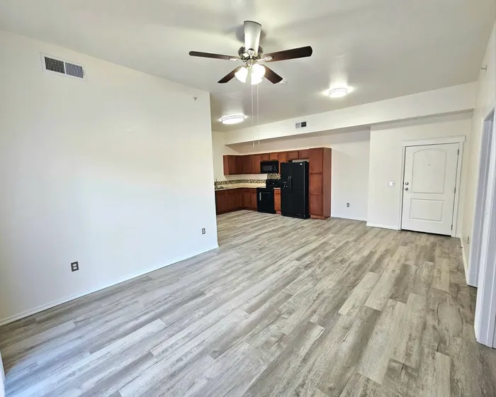 Spacious and modern living area with elegant wood flooring, ceiling fan, and a sleek kitchen with dark appliances and ample cabinetry.