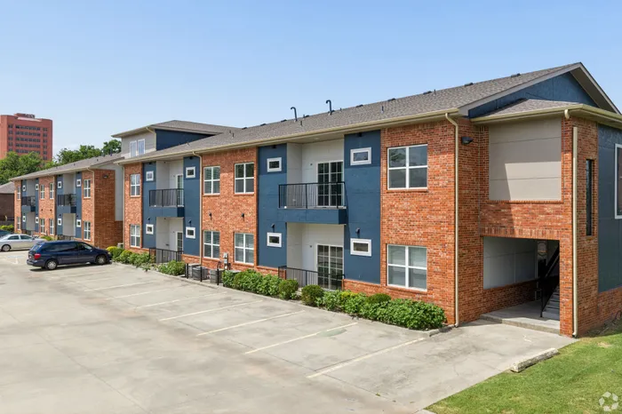 Modern two-story apartment building with elegant brick and blue exterior, featuring private balconies and ample parking space.