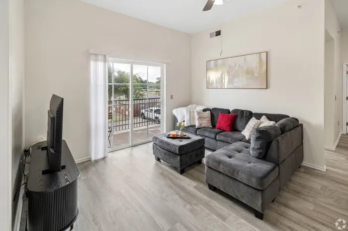 Bright, inviting living room with elegant gray sectional, modern decor, and natural light streaming through sliding glass doors leading to a patio.