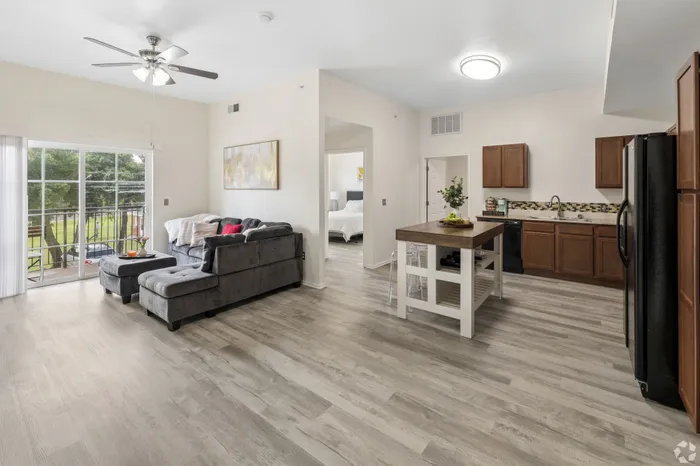 Inviting open-concept living space with modern kitchen, plush gray sectional, and abundant natural light through sliding glass doors.