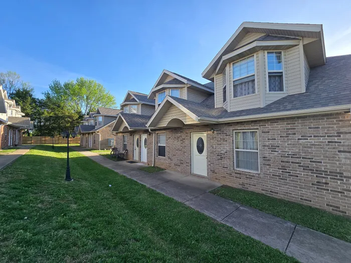 Charming row of townhouses with modern architecture, lush green lawns, and inviting front porches, bathed in morning sunlight.