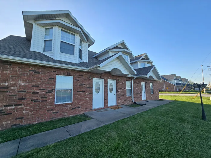 Charming brick apartment complex with inviting white-trimmed windows and doors, set against a clear blue sky.