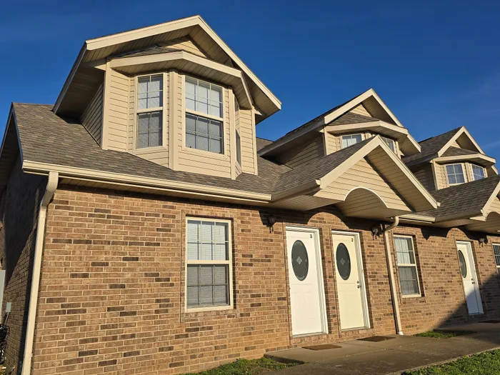 Charming townhouse with classic brick facade and modern dormer windows, basking in sunlight.