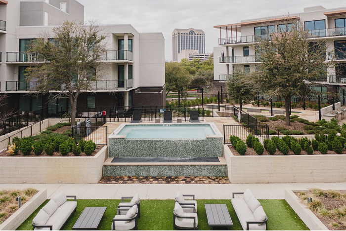 Modern apartment complex with chic outdoor seating, a refreshing pool, and lush landscaping. Cityscape views in the background enhance urban living appeal.
