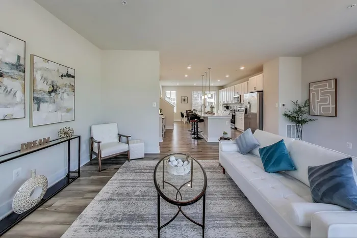 Modern open-concept living space with stylish furnishings, vibrant artwork, and a sleek kitchen featuring stainless steel appliances and high-top seating.