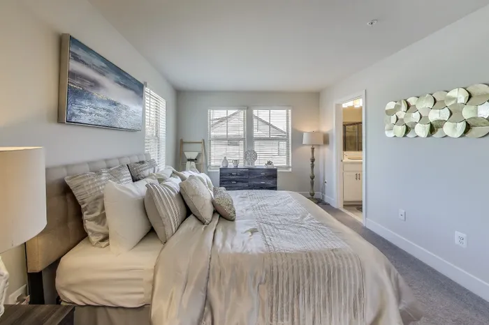 Elegant bedroom with plush bedding, large windows for natural light, and chic decor, featuring modern wall art and a cozy atmosphere.