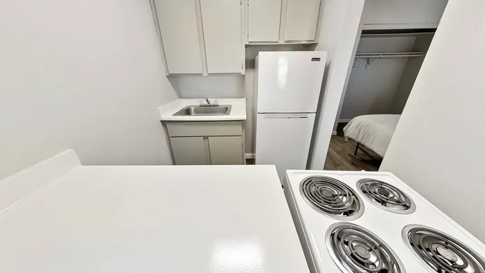 Chic kitchenette featuring a compact fridge, stove, sink, and open view into a welcoming bedroom.