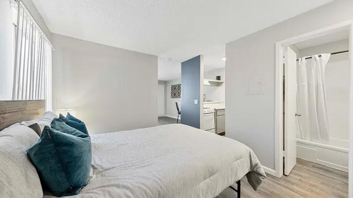 Bright bedroom with elegant decor, plush pillows, and an adjacent open kitchen area.