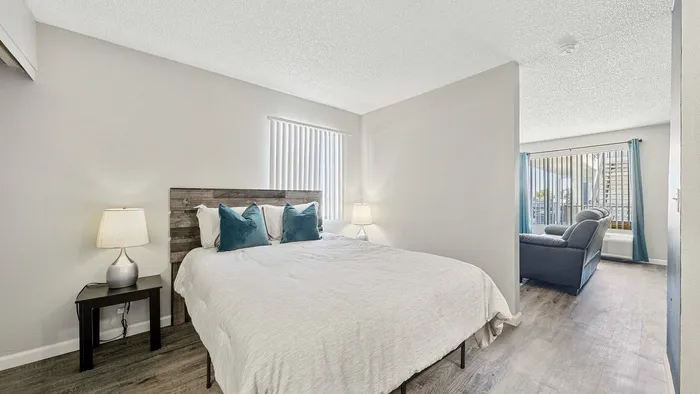 Elegant bedroom with plush bedding, leading to a bright and airy living room.