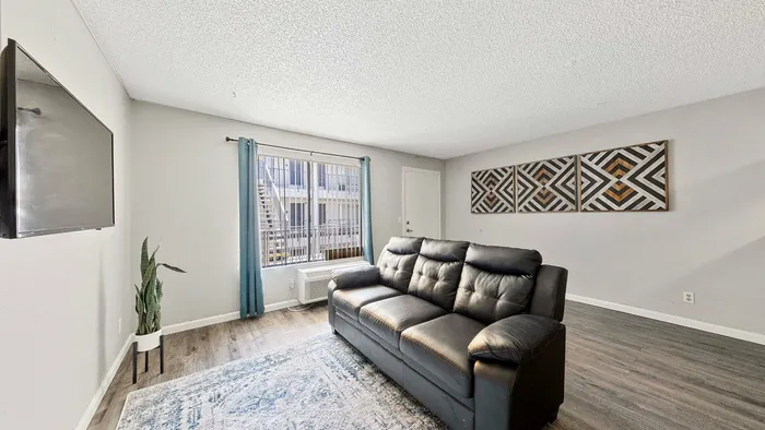 Bright living room with modern decor featuring a sleek black leather sofa, stylish wall art, and a large window with elegant teal curtains.