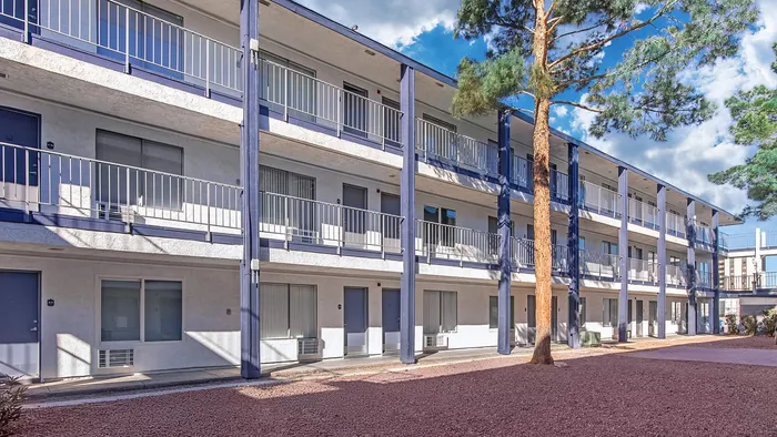 Three-story apartment building with modern balconies and large windows set against a clear blue sky.