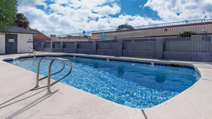 Inviting outdoor pool with clear blue water, surrounded by a sunlit deck and privacy fencing.