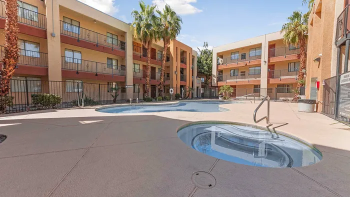 Beautiful apartment complex courtyard featuring a central swimming pool surrounded by palm trees and multi-story buildings.