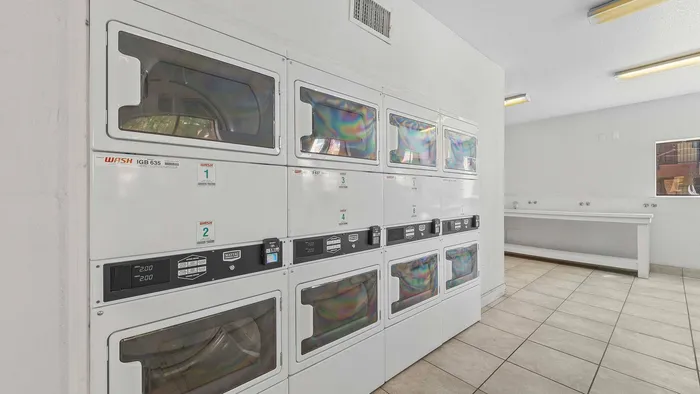 Bright, spacious laundry room featuring multiple modern washing machines in a clean, tiled environment.