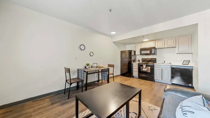 Modern apartment living room with a cozy dining area and sleek kitchen featuring black appliances.