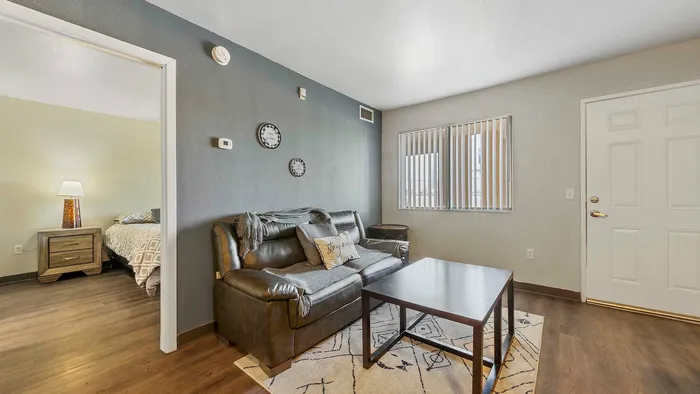 Inviting living room featuring a comfortable leather sofa, modern coffee table, and glimpse into a warmly lit bedroom.