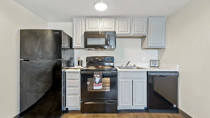 Modern kitchen with black appliances, white cabinets, and wood flooring.