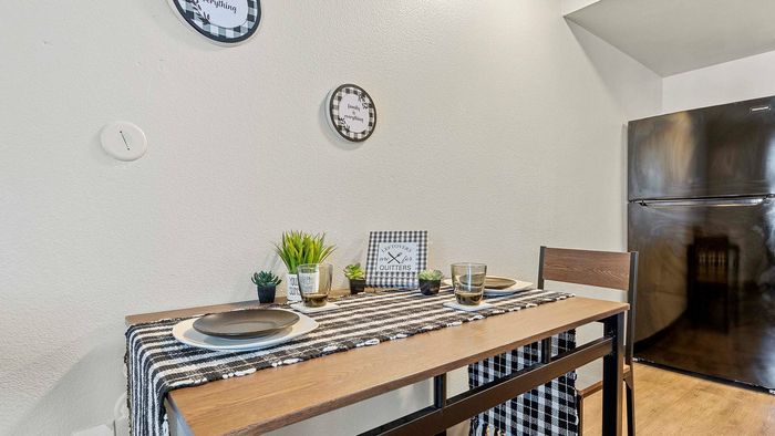 Cozy dining area with a wooden table, black fridge, stylish decor, and succulent plants.