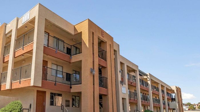 Modern three-story apartment building with balconies and a warm color palette under a clear blue sky.