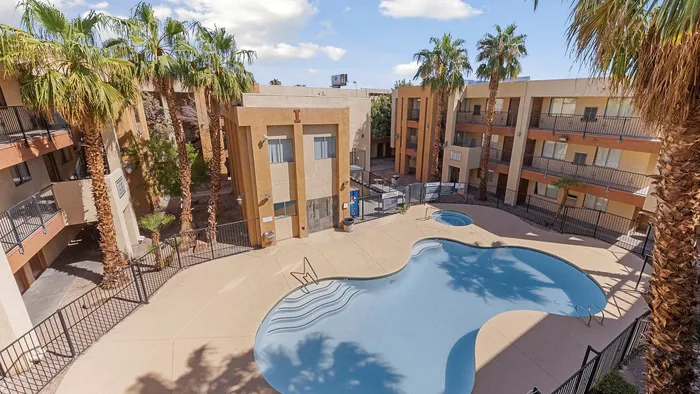 Luxury apartment complex with a serene pool area surrounded by palm trees and three-story buildings.