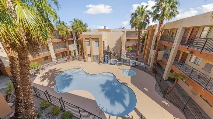 Bright courtyard featuring a central swimming pool surrounded by palm trees and modern apartment buildings.
