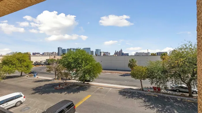 Stunning city skyline view from an apartment balcony with lush green trees and a clear blue sky.