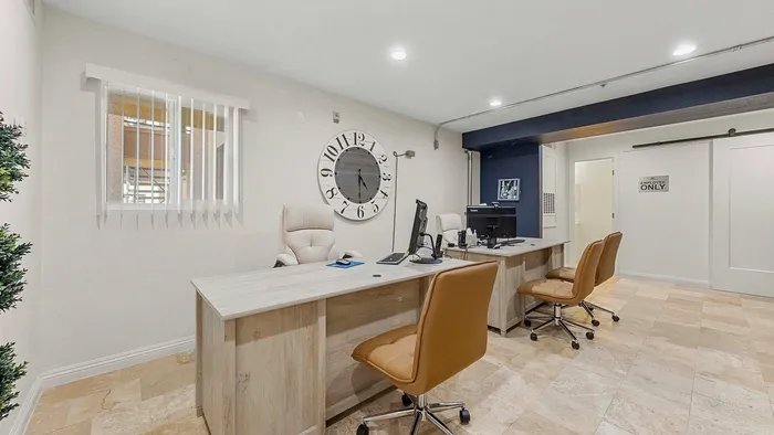 Stylish office area with modern desks and chairs, featuring a large wall clock and ample lighting.