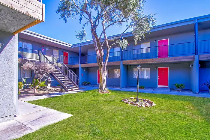 Inviting apartment complex with vibrant red doors, lush greenery, and a spacious courtyard.