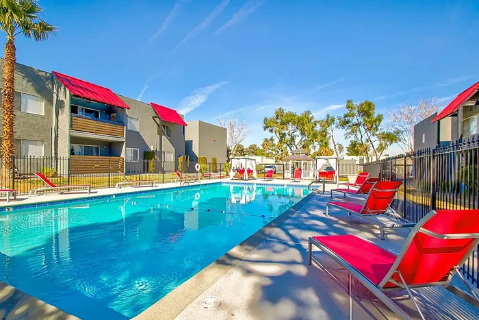Inviting outdoor pool area with vibrant red lounge chairs and modern apartment backdrop.
