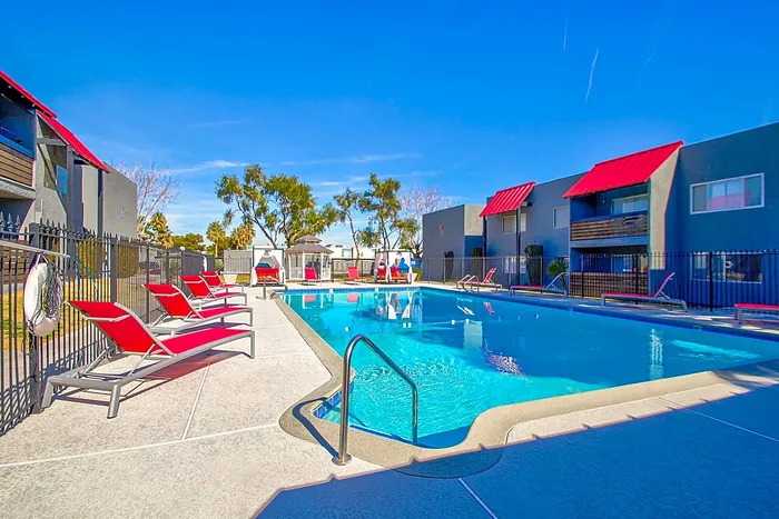 Inviting outdoor pool with red lounge chairs and modern apartment buildings under a clear blue sky.
