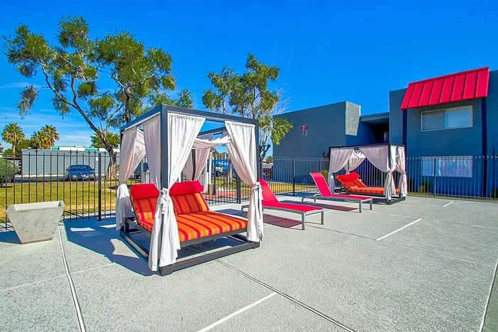 Outdoor lounging area with stylish cabanas and vibrant red lounge chairs under a clear blue sky.