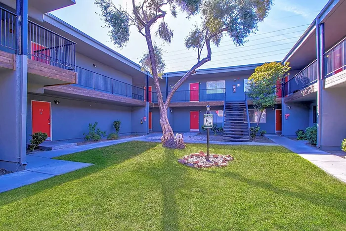 Inviting apartment courtyard with lush green lawn, vibrant red doors, and modern architecture.